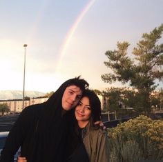 two people standing next to each other with a rainbow in the sky behind them,