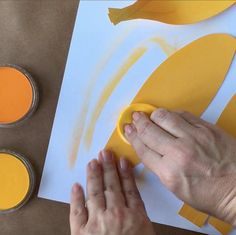 someone is using yellow and orange paint to create banana shapes on paper with other items nearby