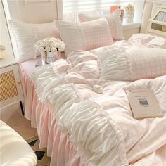 a bed with pink and white comforters in a bedroom next to a book on a table