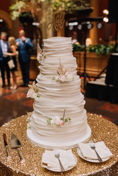 a three tiered wedding cake with flowers on the top is sitting on a table