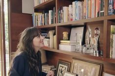 a woman standing in front of a bookshelf with pictures on the shelves behind her