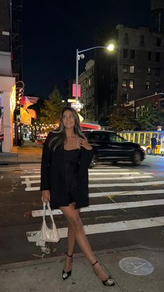 a woman is standing on the street at night with her hand in her pocket and purse