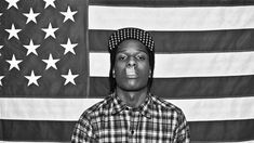 a black and white photo of a man in front of an american flag wearing a hat