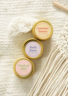 three tins of lip bales sitting on top of a white blanket next to a knitting needle