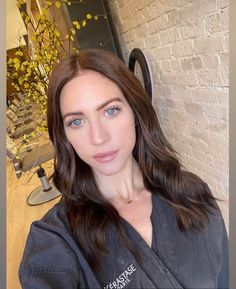 a woman with long brown hair and blue eyes is posing for a photo in front of a brick wall