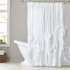 a white bath tub sitting under a window next to a shower curtain with flowers on it