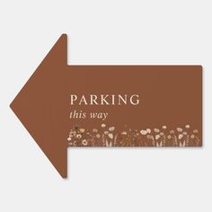 an arrow sign with the words parking, this way and flowers in brown on it