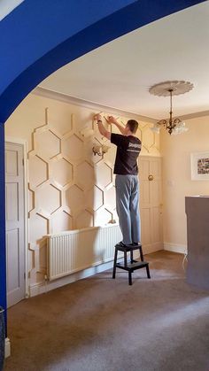 a man standing on top of a stool in front of a blue wall and ceiling