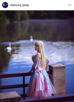 a woman in a pink and blue dress is standing on a bridge near the water