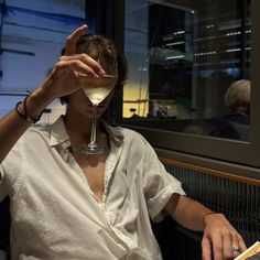 a woman sitting at a table with a wine glass in front of her and a book next to her