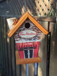 a bird house hanging from the side of a fence with a tin horton sign on it