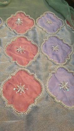 six pink and purple appliques are arranged on a gray cloth with silver beading