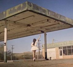 a woman in a white dress is standing under an old gas station with her arms up