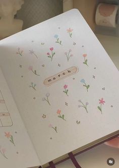 an open notebook with the word march written on it and flowers all over it, sitting on a desk