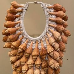 Natural seashell necklace on metal stand. Hand tied on hand knitted back panel.   Necklace dimensions  16.5” wide 26” tall  Metal base 5.5” x 6.25” Indigenous Jewelry, Baroque Jewelry, Shell Jewellery, Wood Fashion, Cowrie Shell Necklace, Pearl Drop Necklace, Pearl Jewels, She Sells Seashells, 3d Craft