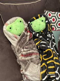 two stuffed animals wrapped in blankets on a couch