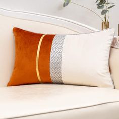 an orange and white pillow sitting on top of a couch next to a potted plant