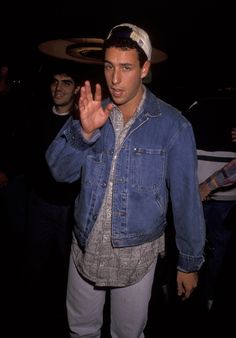 a man standing in the dark with his hand up and wearing a denim jacket over his shoulders