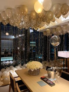 a room filled with lots of balloons hanging from the ceiling and white flowers in a vase