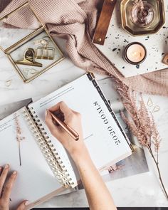 a person is writing on a notebook next to some candles and other items that are scattered around the table