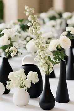 black and white vases are lined up on a table with flowers in each one