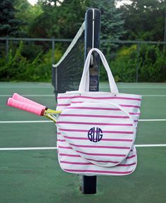 a pink and white striped tote bag with a monogrammed tennis racket sticking out of it