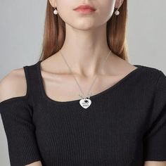 a woman wearing a black top and silver necklace with a heart shaped pendant on it