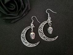 This beautiful earring set is handmade with mystique and wonder. Dainty skulls hang from an antique silver crescent moon, adding a touch of macabre elegance to any outfit. These earrings are a subtle statement piece and a fun conversation starter. Total length of the earrings with the hooks hang at approximately 3" inches. For longevity, it is recommended to steer clear of water and store in an air-tight container. The colors of the piece may vary slightly depending upon your monitor settings.  ------- Shipping: Ground Advantage (within the US) including tracking number Please visit http://www.etsy.com/shop/shaireproductions for more pieces. Thanks for looking!! © Design by Sherrie Thai of Shaireproductions.com. Copyrights are not transferrable with the sale of the item. Feel free to conne Bohemian Sterling Silver Skull Jewelry, Gothic Skull Earrings, Silver Gothic Dangle Jewelry, Gothic Skull Earrings For Halloween, Gothic Skull Shaped Pierced Earrings, Bohemian Skull Earrings For Gifts, Handmade Silver Gothic Jewelry, Handmade Gothic Silver Jewelry, Adjustable Gothic Skull Earrings