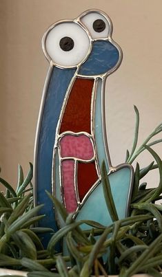 a stained glass bird sitting on top of some green grass with eyes and beaks