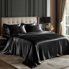 a bed with black sheets and pillows next to a window in a dark colored room