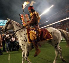 a man riding on the back of a white horse next to a crowd at a football game