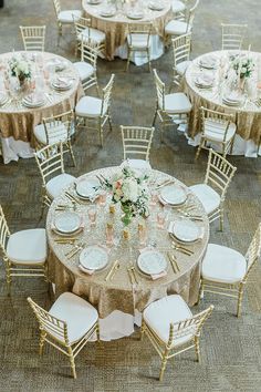 an overhead view of a table set with gold linens and white chairs, topped with floral centerpieces