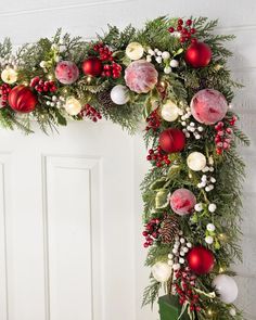 a christmas wreath with ornaments and greenery hanging from the front door, decorated in red white and green