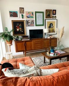 a living room with orange couches and pictures on the wall above them, along with a coffee table