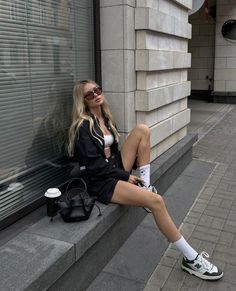 a woman sitting on the side of a building with her legs crossed and wearing white socks