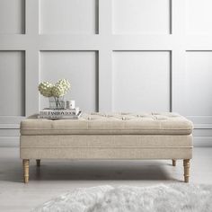 a white room with a bench and flowers on it's end table in front of a paneled wall