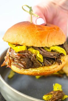 a hand holding a sandwich with meat and mustard