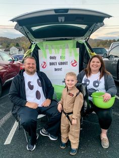 two adults and a child sitting in front of a car trunk