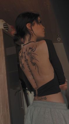 a woman with a tattoo on her back standing in front of a counter top oven