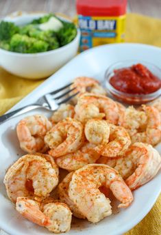 a white plate topped with shrimp and broccoli next to a bowl of ketchup