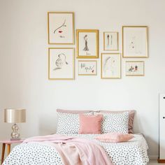 a bedroom with white walls and pictures on the wall above the bed, along with a pink blanket