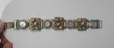 "Vintage linked bracelet of rectangular and round shaped sections. The rectangle links have what looks like semi precious stones of turquoise, pearls and agate. Very detailed scrolled design. The round links are inlayed with mother of pearl. All links are connected with cylindrical joints. This piece falls nicely around the wrist. Some discoloration to the metal although it is a very well made piece. Measurement: 7 3/4\" X 1\" ALL SALES FINAL. NO RETURNS OR EXCHANGES. PLEASE ASK ALL QUESTIONS AH Gold Rectangular Bohemian Bracelets, Handmade Metal Rectangular Bracelets, Handmade Rectangular Metal Bracelets, Bohemian Jeweled Bracelets For Formal Occasions, Bohemian Jeweled Bracelet For Formal Occasions, Vintage Rectangular Bracelet Strap Jewelry, Vintage Square Metal Jewelry, Vintage Stone Bracelets As Gift, Vintage Stone Bracelet For Gift