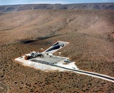 an aerial view of a large building in the middle of some desert with mountains behind it