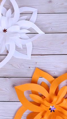 two paper flowers sitting next to each other on a wooden surface with one flower cut out