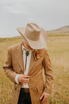 a man wearing a tan suit and hat standing in the middle of an open field