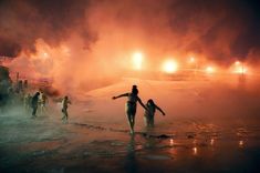 some people are walking in the water with their surfboards and glowing lights behind them