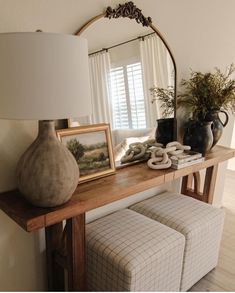 a table with a mirror, vases and other items on it next to a lamp