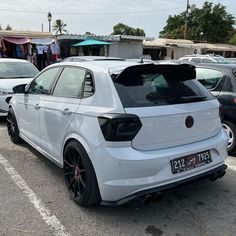 the rear end of a white car parked in a parking lot next to other cars