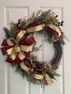 a christmas wreath on the front door with red and gold ribbons hanging from it's sides