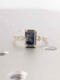 a black diamond ring sitting on top of a silver surface with three diamonds around it